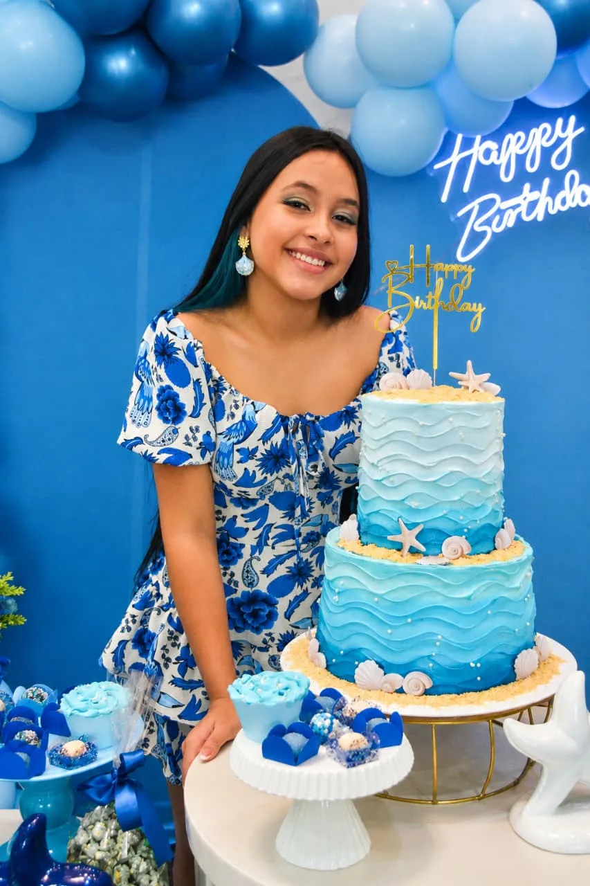 Mulher sorrindo atrás de um bolo azul em festa de 15 anos